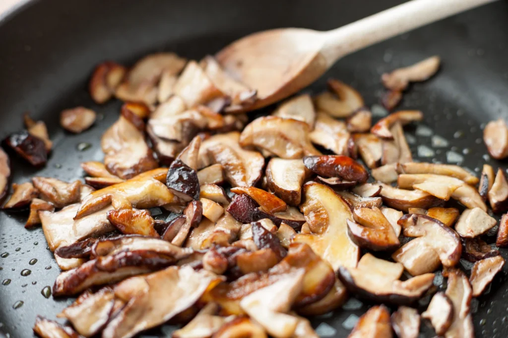 Funghi tagliati a piccoli pezzi che rosolano in una padella scura con una spatola di legno