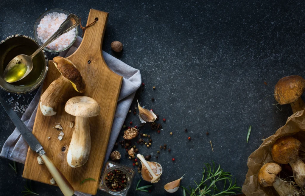 Funghi porcini interi e tagliati accanto a un coltello e un tagliere su una superficie scura