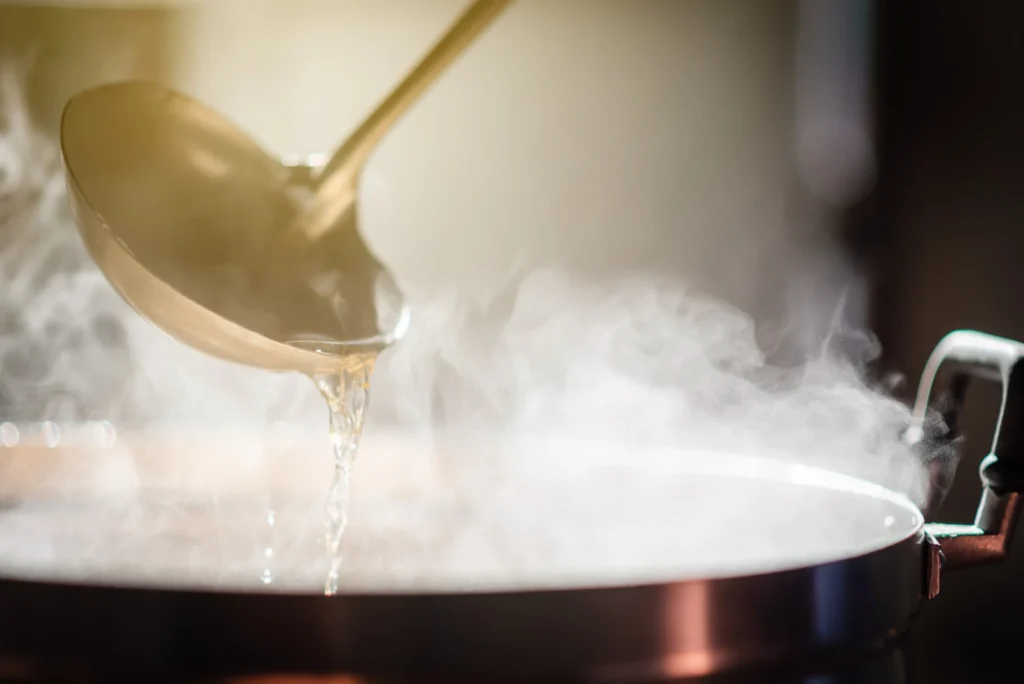 Mestolo metallico che versa del liquido caldo e fumante sopra una pentola