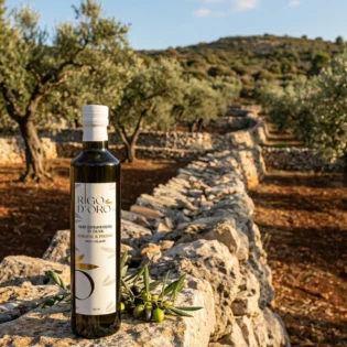 Bottiglia Rigo D'Oro 100% Italiano appoggiata su un muretto in pietra davanti a un uliveto