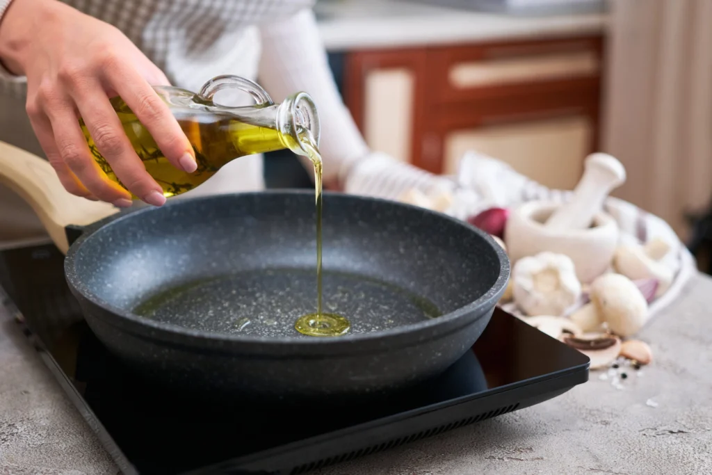 Una mano versa olio da una bottiglietta di vetro in una padella accanto a funghi freschi