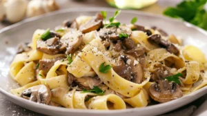 Pappardelle servite nel piatto con pezzi di funghi, erbe e condimento cremoso