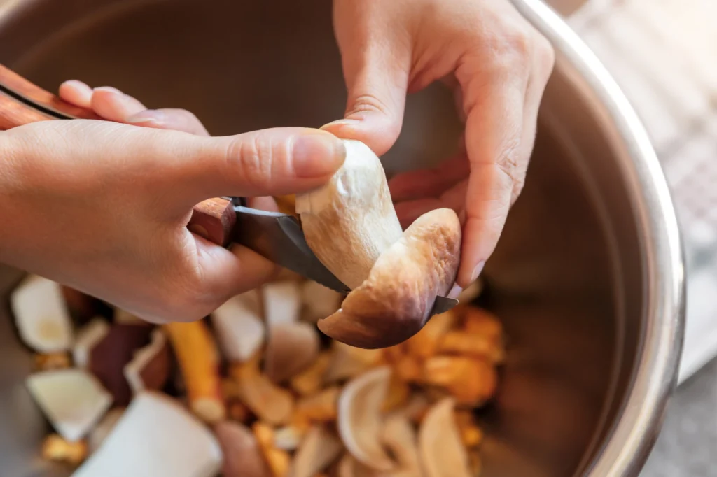 Mani che puliscono delicatamente un fungo sopra una ciotola con altri funghi