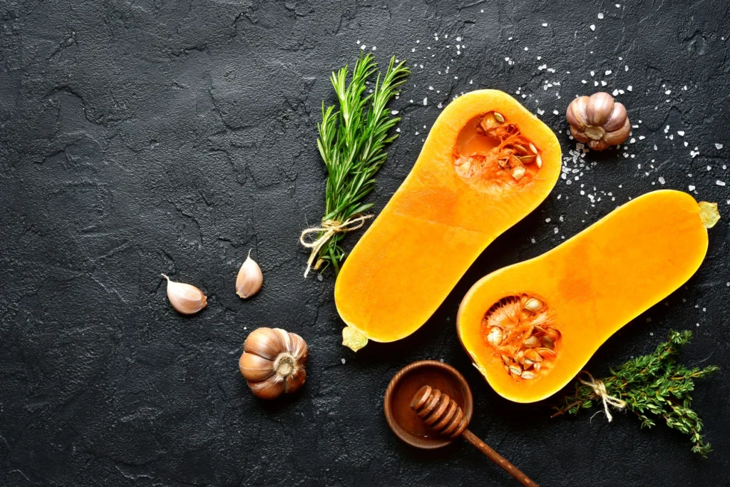 Zucca violina divisa a metà e a fette su una superficie scura con rosmarino e altri ingredienti